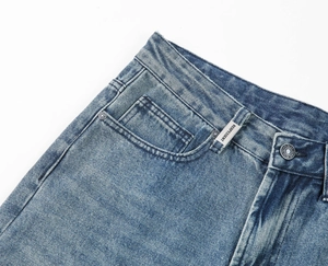 Detailed macro shot of light blue washed denim waist, metal buttons, and silver brand tag