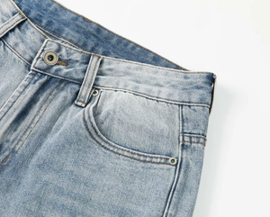 Dettaglio della vita con bottone in metallo e rivetto su jeans lavati blu chiaro a gamba dritta