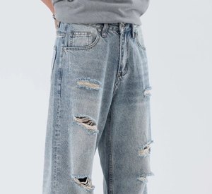 Close-up of light blue washed denim jeans featuring distressed ripped details and whiskers