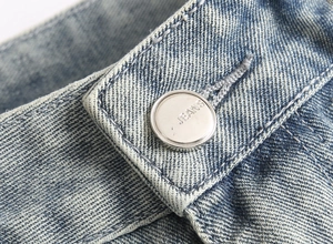 Detailed macro view of light blue washed denim waist with silver metal JEANS button