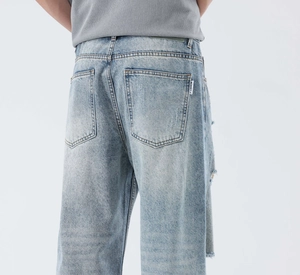 Detail view of light blue washed jeans with frayed fringe rip and fashion label on back pocket