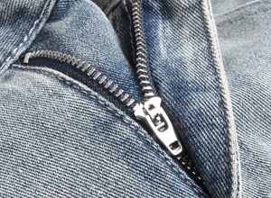 Macro view of a durable silver metal zipper on premium blue denim fabric shorts