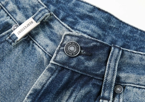 Detailed macro view of the light blue wash denim texture with metallic brand tag and button
