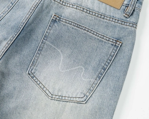 Dettaglio della tasca posteriore dei jeans con logo a gabbiano bianco e patch in pelle marrone