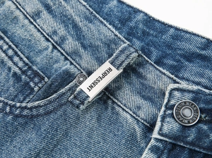Macro shot of heavy washed denim texture with branded metal button and belt loop detail