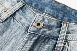 Dettaglio macro del bottone metallico e cuciture gialle su jeans blu lavati