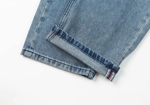 Detailed close-up of light wash denim jeans featuring red and white selvedge hem stitching