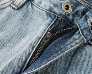 Dettaglio dei jeans con cerniera in metallo YKK e chiusura con bottone in bronzo vintage