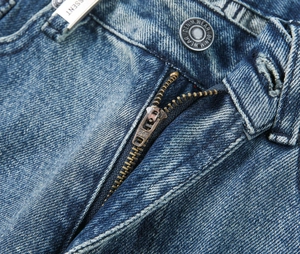 Macro shot of light blue denim jeans showing YKK zipper and branded metal button detail