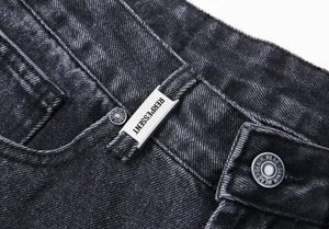 Gros plan sur la taille en denim noir délavé avec plaque logo argentée et bouton gravé