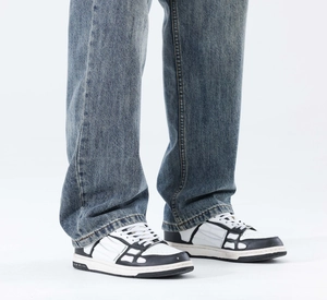 Détail du jean bleu clair délavé porté avec des chaussures à motif squelette de style Amiri
