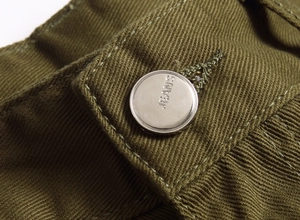 Vue macro du bouton métallique argenté gravé JEANS sur le tissu denim de couleur olive