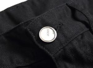 Détail du bouton en métal argenté gravé JEANS sur un tissu denim noir de qualité