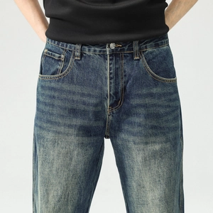Détail macro du jean en denim bleu délavé vintage pour homme avec coutures orange et bouton