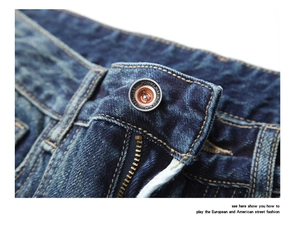 Macro shot of bronze metal button and zipper detail on heavy wash dark blue denim pants