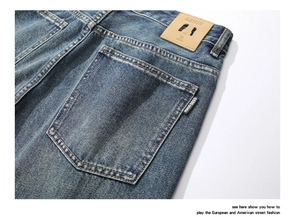 Detail of dark blue washed denim jeans featuring yellow stitching and a leather patch