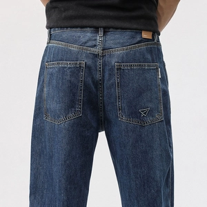 Detail of dark blue washed denim jeans with a paper plane embroidery on the back pocket