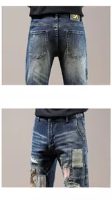Detail view of distressed denim jeans with heavy embroidery, patches and leather brand tag