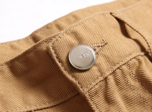 Détail macro d'un short en jean kaki montrant un bouton métallique gravé du mot JEANS