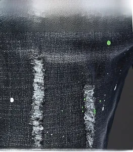 Détails macro du tissu denim déchiré avec éclaboussures de peinture verte et effilochage