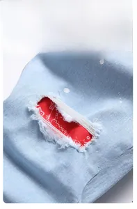 Detail of light blue jeans featuring knee distress with red paisley patch and white paint drips