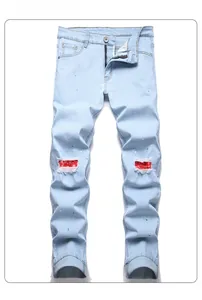 Close-up of ripped denim jeans featuring red paisley patches and green paint splatters