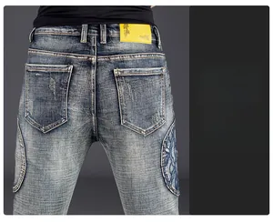 Detail of dark blue denim jeans featuring intricate blue floral embroidery and cat whisker fading