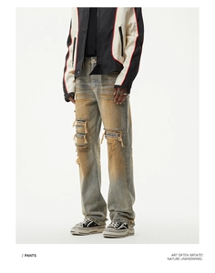 Detail of ripped straight-leg jeans featuring vintage dirty wash and striped patchwork