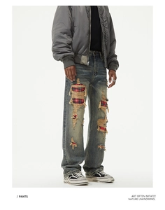 Close-up of distressed denim jeans featuring vintage wash and red plaid patch details