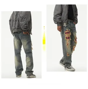Detail of distressed denim with red plaid patches on loose-fit vintage wash jeans