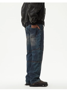 Detail showing vintage washed blue denim texture and horizontal stitching on trousers