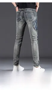 Detail of slim-fit distressed denim jeans with vintage blue embroidery and ripped patches