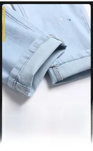 Close-up of light blue jeans leg with green paint splatters and cuffed hem detail
