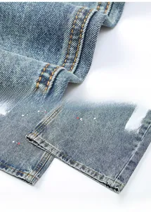 Détail d'un jean vintage délavé avec des surpiqûres orange et des éclaboussures de peinture