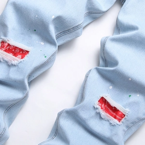 Men's light blue distressed jeans with red bandana knee patches and colorful paint drips