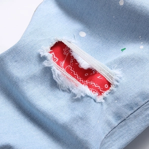 Men's light blue distressed jeans featuring red paisley patch and white paint splatter