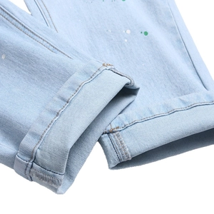 Men's light blue distressed jeans with creative green paint splatters and cuffed hems