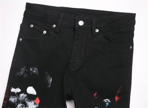 Detail of black distressed jeans featuring artistic paint splatter and metal button hardware
