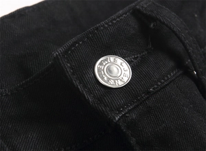 Macro shot of silver metal button with JEANS engraving on black distressed denim jeans