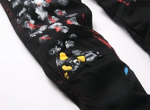 Macro detail of street-style black jeans featuring vibrant paint splatter and knee paneling
