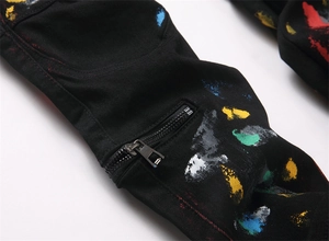 Close-up of black denim jeans featuring colorful paint splatters and metal zipper detail