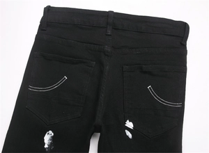 Detail of men's black street jeans featuring white ink splatter and arc pocket stitching