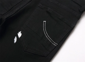 Detail of black distressed denim jeans with back pocket embroidery and white paint splatters