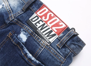 Detail shot of distressed blue denim jeans showing the logo leather patch and stitching