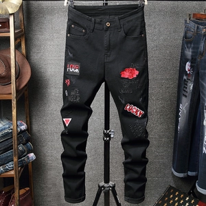 Detail of red rose embroidery and street style graffiti print on slim black denim jeans
