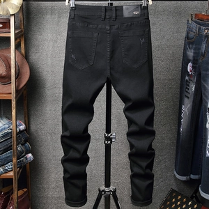 Detail of black slim fit jeans featuring back pocket distressing and a leather waist patch
