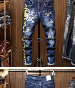 Detailed view of white tiger embroidery and yellow lettering on blue distressed jeans