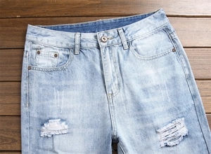 Détail d'un jean bleu clair vieilli avec déchirures faites main et texture denim lavé