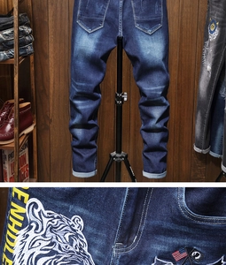 Detail of tiger head embroidery and washed texture on dark blue straight denim jeans