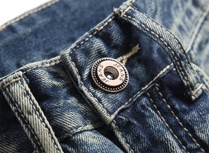 Detaillierte Nahaufnahme des Bronze-Knopfes an dunkelblauer Jeans mit gelben Kontrastnähten